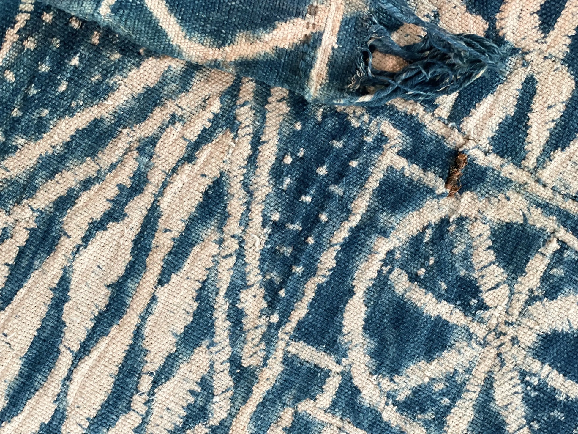 Détails du plaid indigo en ndop vintage pur coton - 1ère pièce de la collection NAMTCHEMA par Studio Matongé qui rassemble une série de pièces uniques confectionnées à la main à partir de pièces de ndop vintage chinées. Ici une couture en raphia très serrée permettant de créer les motifs blancs lors de l'étape de teinture. Émouvante preuve de l'authenticité et du caractère vintage de notre pièce. 