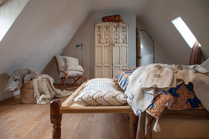 Dans la chambre à coucher, sur le lit couvre-pied en wax et double gaze de coton - FUNTENI, plaid  Studio Matongé en bogolan blanc LENGO, plaid en laine écru TANGGOOR. 
Sur le bout de lit en rafia, combinaison de housses de coussin en bogolan écru faites main, DOTS, WEX, TAAR, en format carré 50 x 50 cm. 
Sur la chaise housses de coussin en bogolan MSINGI en 50 x 50 cm et TAAR 30 x 50 cm
Dans le panier en osier, maxi hippopotame RAYMOND en laine fait main.