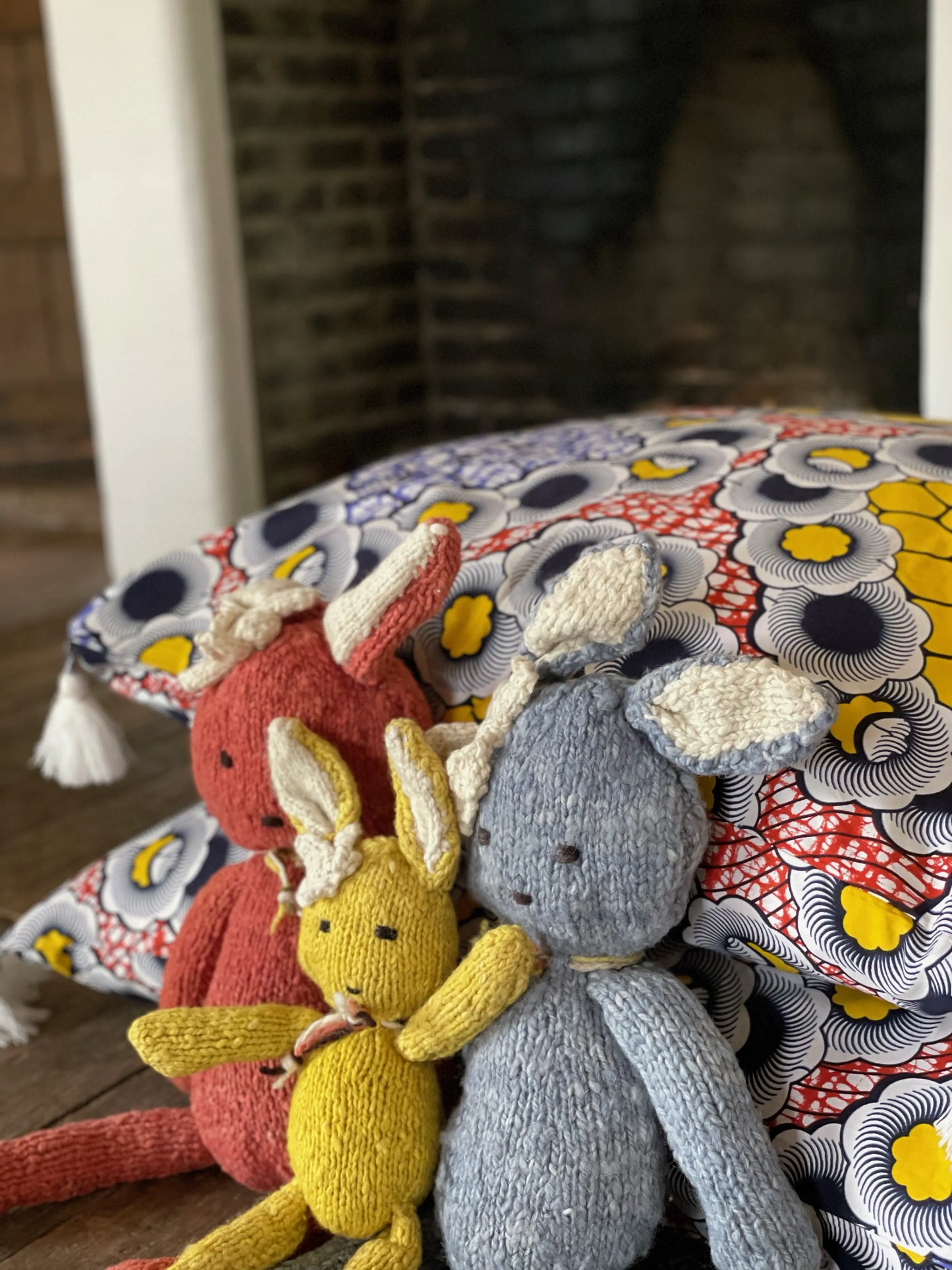 Famille de doudous SIMONE, notre peluche lapin ici en  jaune, bleu et corail en tailles S et L, en laine bio faite main éco-responsable. Le doudou lapin SIMONE est disponible en 2 tailles et plusieurs couleurs chez Studio Matongé.
Ici avec la housse de coussin en wax SOGIN en 80 x 80 cm.