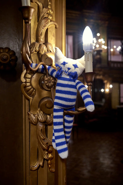 Notre peluche chat rayé blanc et bleu à longues pattes fait son show au théatre de la Monnaie à Bruxelles. Modèle MALO, fait main par la coopérative Kenana Knitters. En coton bio tout doux certifié GOTS. Utilisable dès la naissance.