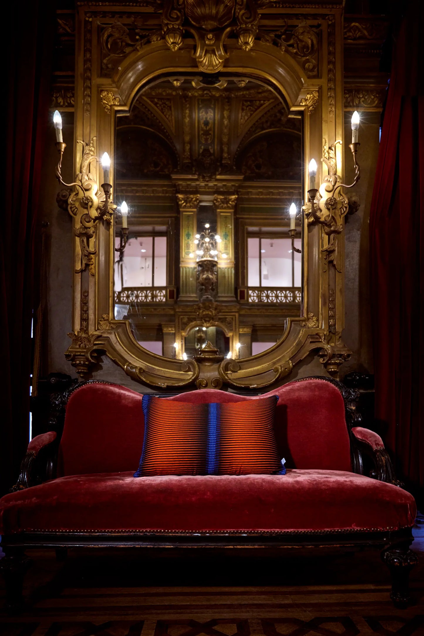 Dans les magnifiques décors du grand foyer de l'Opéra de la Monnaie de Bruxelles, housse de coussin en wax et lin - AGU - Studio Matongé. Fait main en Belgique. Versatile, notre coussin bi-matière s'adapte à vos envies : une face en wax coloré et une face unie en épais lin marine