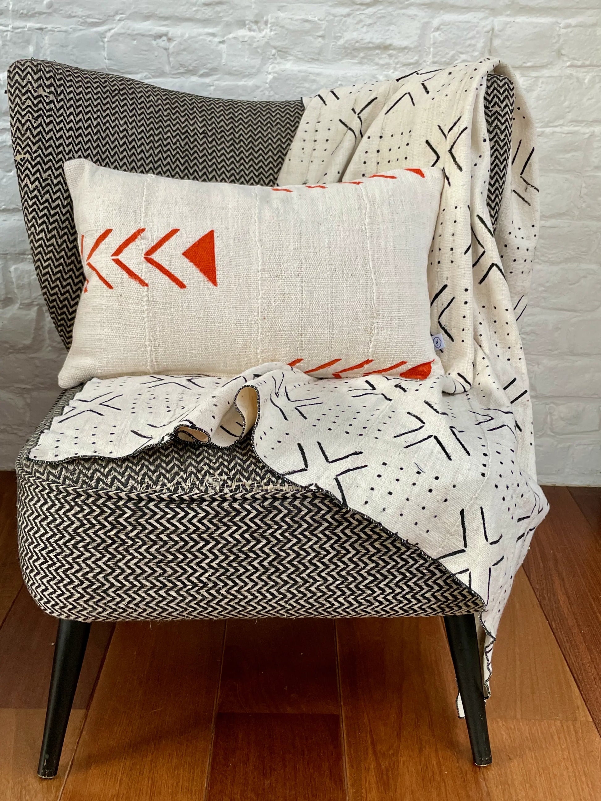 Sur un fauteuil à chevrons, plaid blanc en bogolan pur coton bio tissé main  MSALABA et housse de coussin UPENDO par Studio Matongé